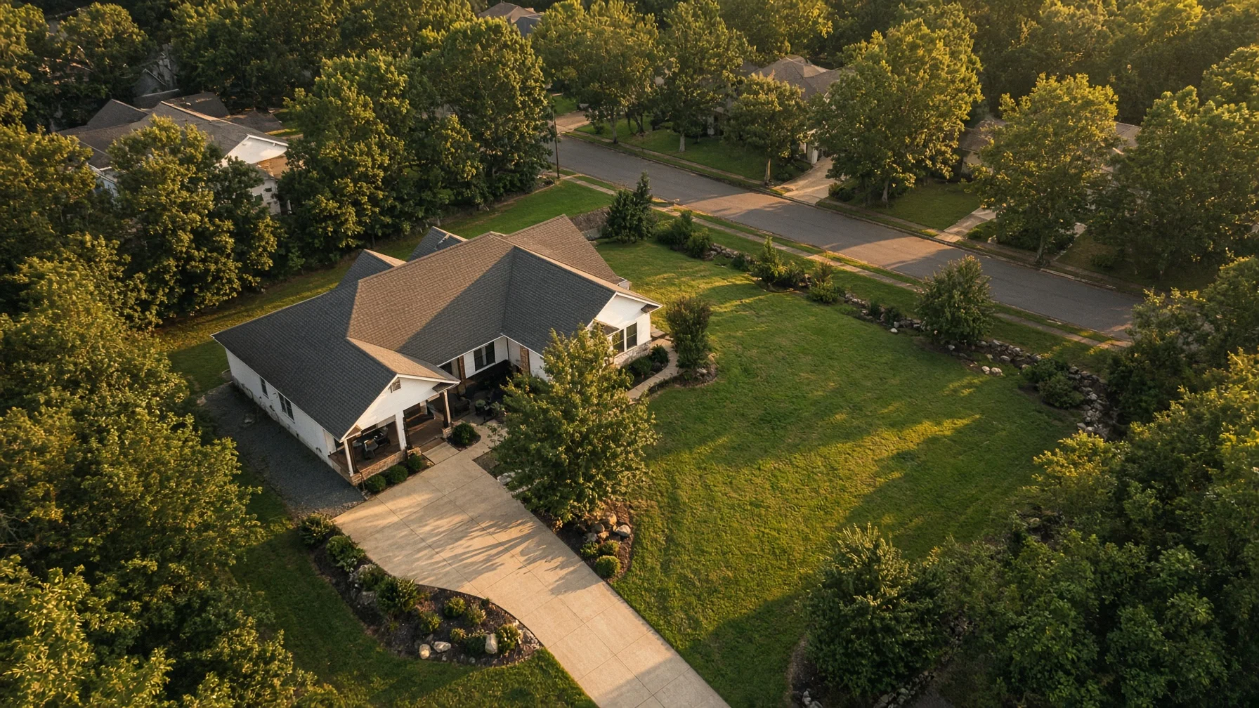 Angled drone view showing a home, yard, driveway, and surrounding property context